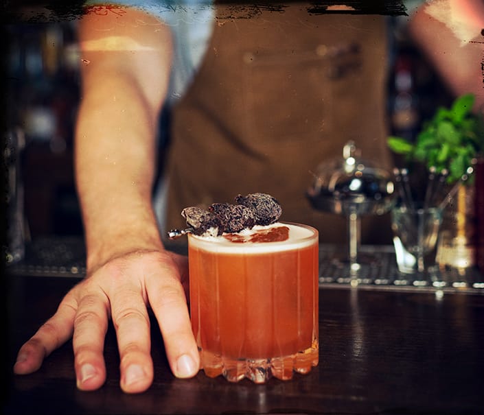bartender serving red orange marooned at sea whiskey cocktail with ice and fig garnish