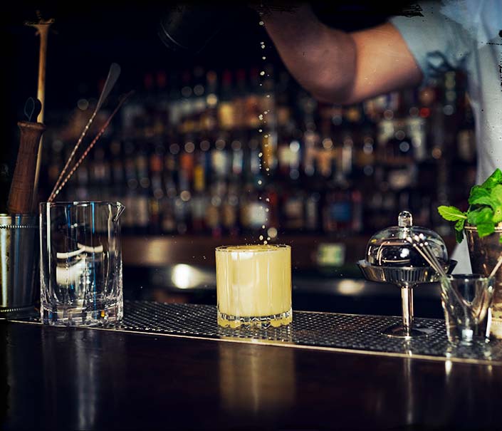 bartender making orangano whiskey cocktail in rocks glass with shaker strainer